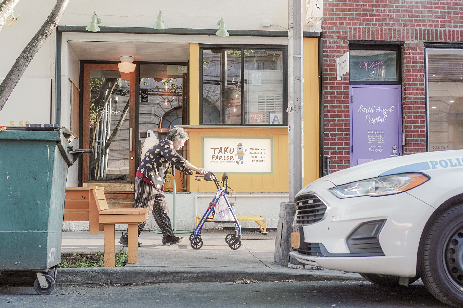 An older New Yorker walking past a colorful neighborhood storefront with a mobility walker